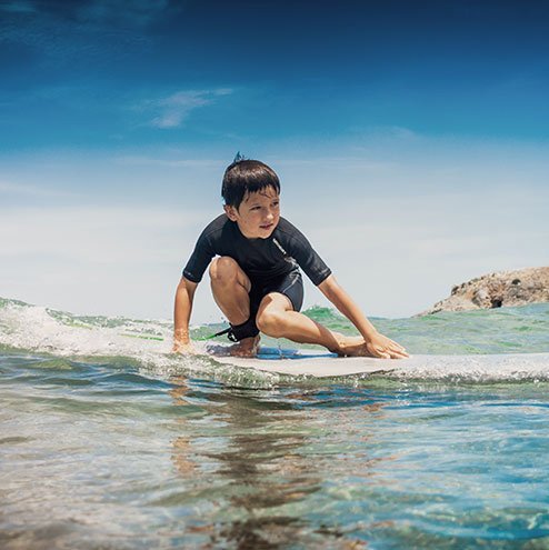 ein kleines Kind surft im Meer.