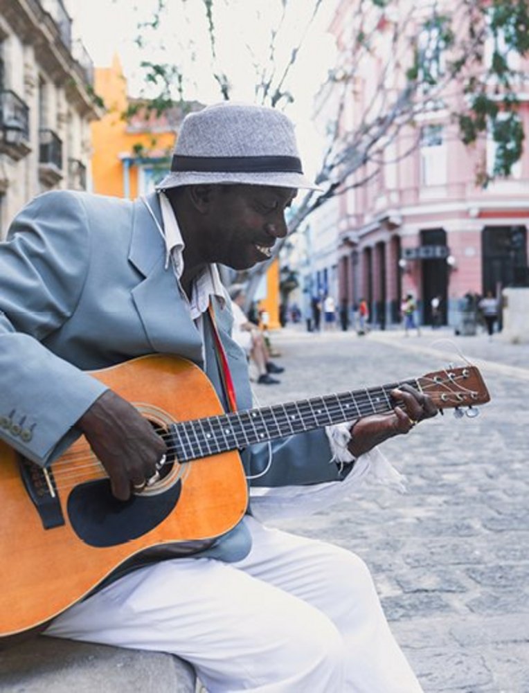 Ein Mann spielt akustische Gitarre an einer Straßenecke und verbreitet karibisches Flair.