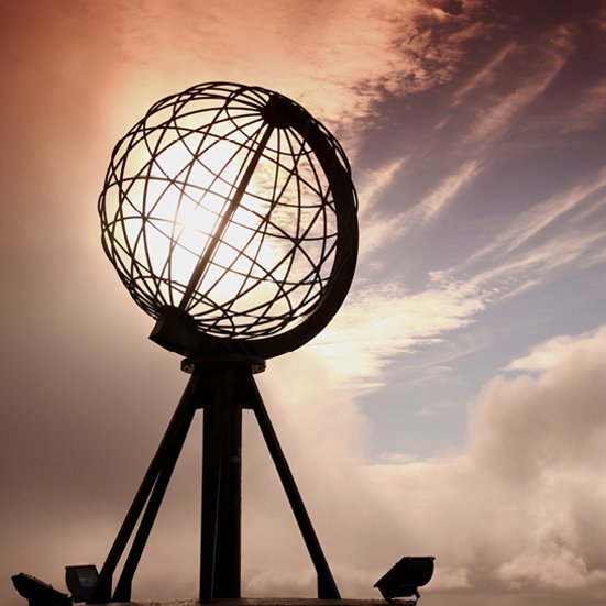 Ein Globus auf einem Pfahl mit der Sonne im Hintergrund, aufgenommen am Nordkap.