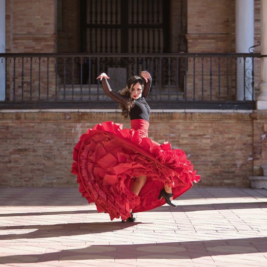 Eine Frau in einem roten Rock tanzt vor einem Gebäude in Spanien.