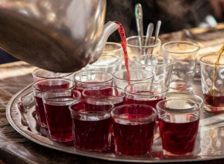 Hibiscus tea being poured from a metal kettle into small tea glasses