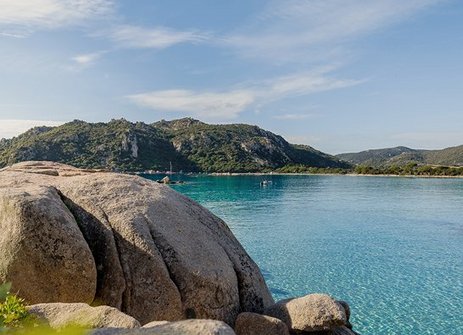 Eine Person sitzt auf einem Felsen und schaut auf ein ruhiges Gewässer.