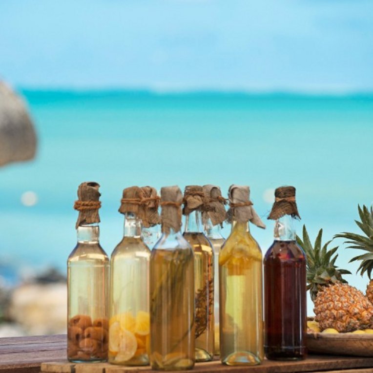 Glas bottles filled with different rum types in front of the ocean