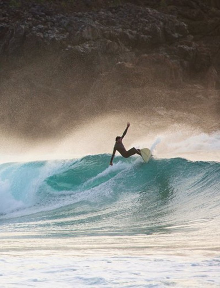 Surfer reitet eine Welle auf Fuerteventura, umgeben von klarem Wasser und strahlendem Himmel.
