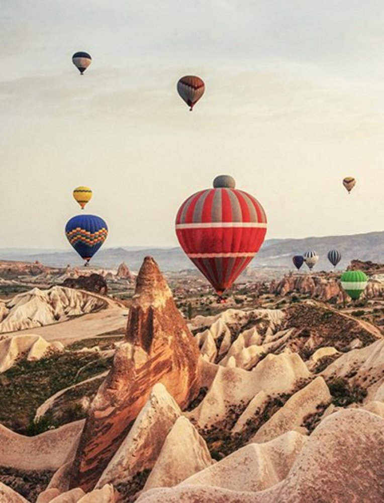 Viele Heissluftballons schweben über die felsige Landschaft von Kappadokien.