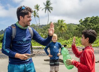 Gruppe von Jugendlichen mit verantwortlichem Mann der Blue Warriors-Initiative geben sich High Five nach Beach Clean Up