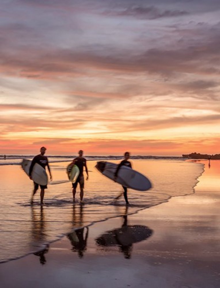 Drei Surfer gehen am Strand bei Sonnenuntergang auf der Nicoya-Halbinsel in Costa Rica.