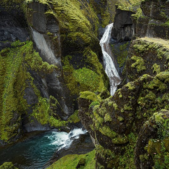 Ein Wasserfall fliesst über eine felsige Klippe im Fjadrárgljúfur in Island.