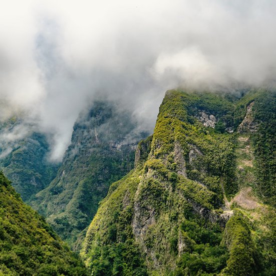 Gebirgskette mit üppigem Grün und Wolken, die den Himmel bedecken.