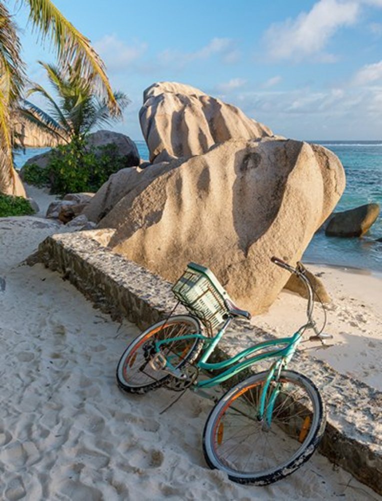 Am Strand der Seychellen parkt ein Vélo neben einem imposanten Felsen.