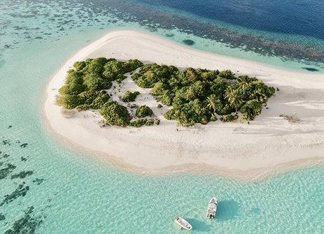 Luftaufnahme einer maledivischen Insel mit einem Boot im Wasser, umgeben von klarem, blauem Ozean.