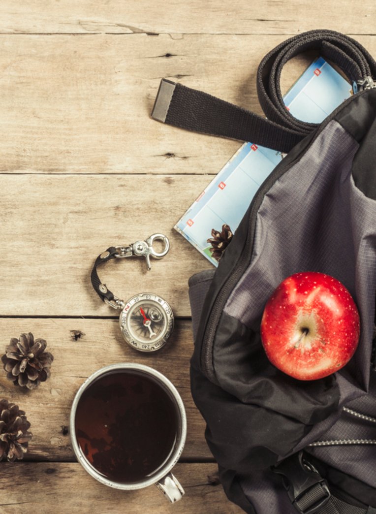 Auf dem Tisch liegt eine braune Reisetasche, einen Kompass, ein Apfel und eine Tasse Kaffee