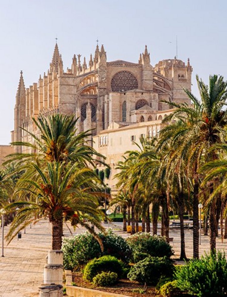 Grosses Gebäude mit einem Uhrturm im Hintergrund, typisch für die Architektur auf Mallorca.