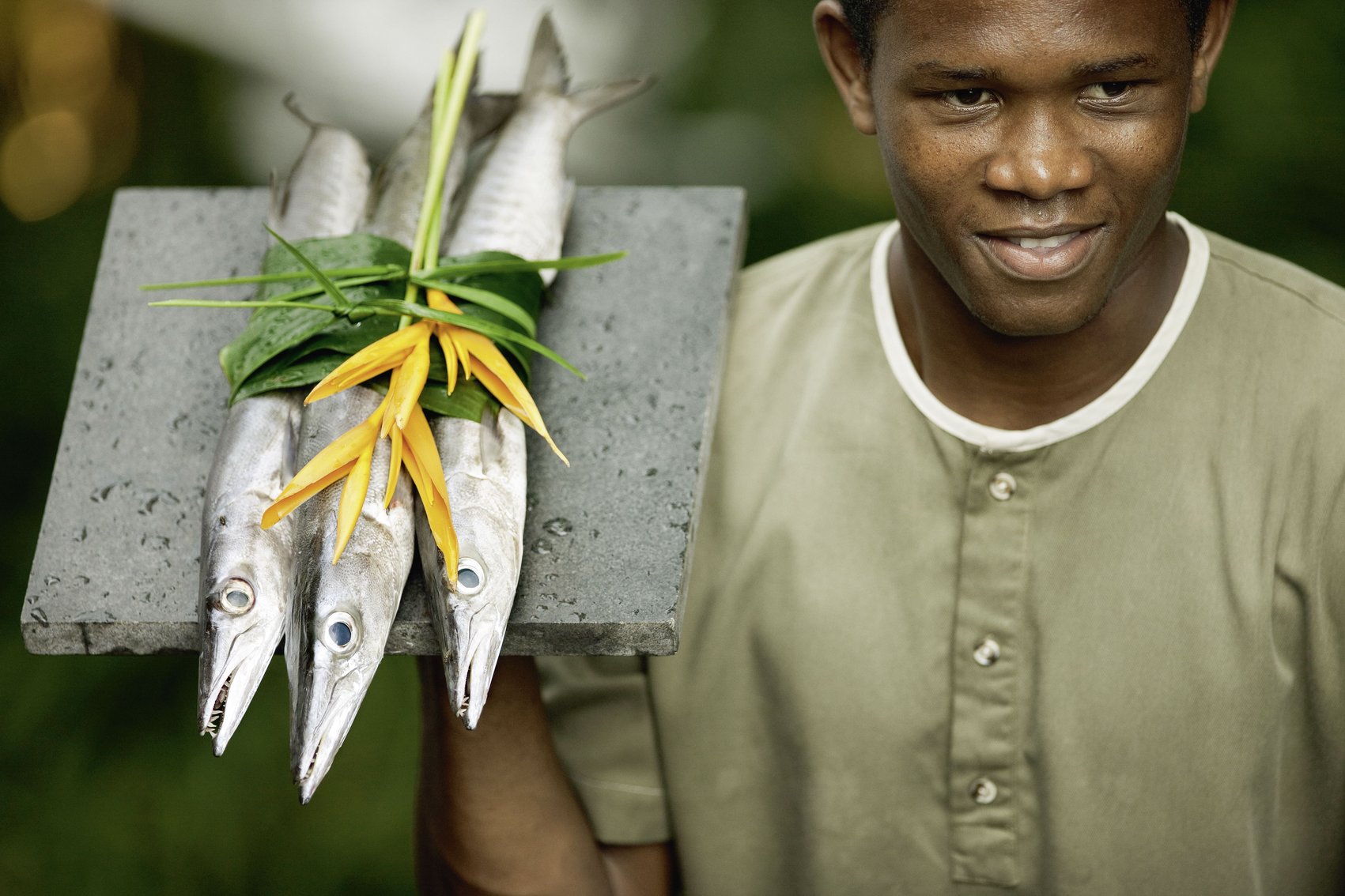 Ein Mann hält ein Tablett mit frischem Fisch und Blättern auf den Seychellen.
