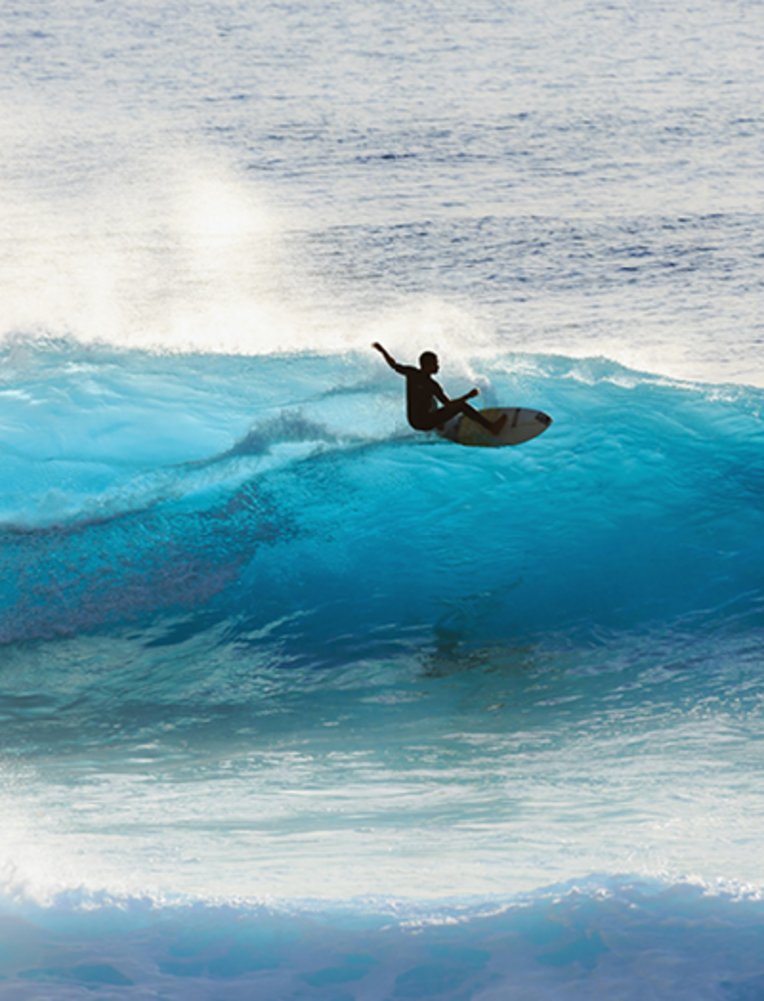 Silhouette eines Surfers, der auf der Insel Madeira, Portugal, einem beliebten Reiseziel für Surfer, auf den grossen blauen Wellen reitet.