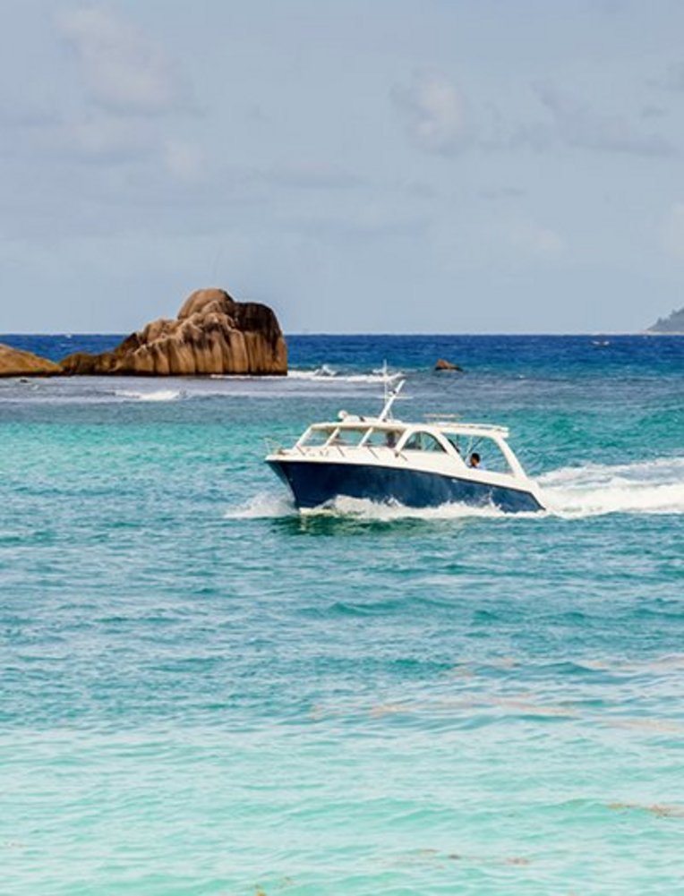 Ein Boot fährt durch das Wasser der Seychellen, umgeben von klarem, blauem Ozean und tropischer Landschaft.