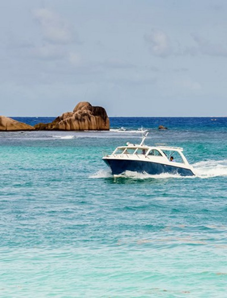 Ein Boot fährt durch das Wasser der Seychellen, umgeben von klarem, blauem Ozean und tropischer Landschaft.