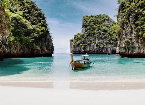 Ein Boot liegt am Strand nahe einer felsigen Küste in Phuket, Thailand, mit Blick auf die Koh Phi Phi Inseln.