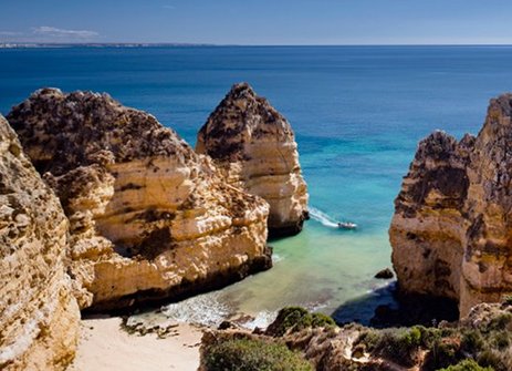 Die Klippen am Strand in Portugal, mit sanften Wellen und klarem Himmel im Hintergrund.