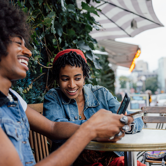 Un homme et une femme assis à une table à NYC, regardant un téléphone portable ensemble.