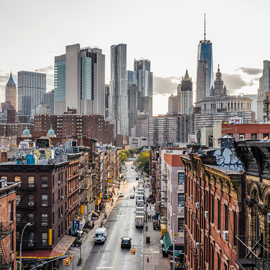 Vue du skyline de New York depuis un toit, avec des gratte-ciels emblématiques sous un ciel bleu.