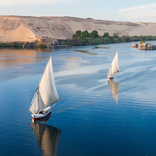 Deux voiliers naviguant sur le Nil en Égypte, avec des reflets scintillants sur l'eau calme.