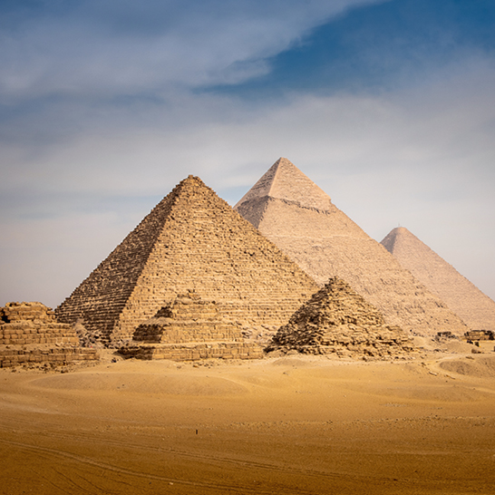 Les grandes pyramides de Gizeh, Égypte, se dressent majestueusement sous un ciel bleu clair.