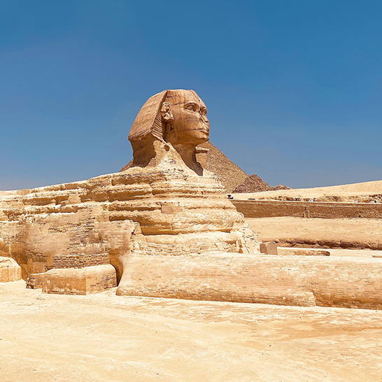 Grande statue de sphinx dans le désert, avec le Caire en arrière-plan, sous un ciel bleu clair.