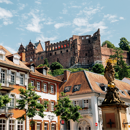 Blick auf die Heidelberger Altstadt mit farbigen historischen Häusern und dem darüber thronenden Schloss auf dem Hügel.