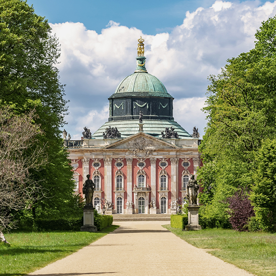 Neues Palais im Park Sanssouci in Potsdam, mit grosser Kuppel, barocker Fassade und breitem Weg zwischen gepflegten Rasenflächen.