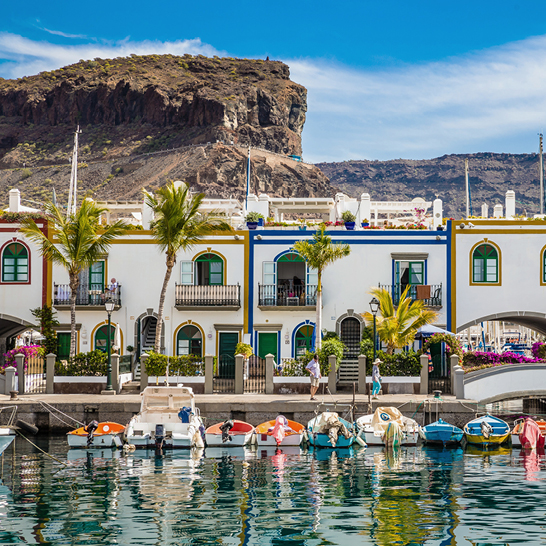 Une rangée de bateaux dans le port de Puerto de Mogán, à Grande Canarie, avec de majestueuses montagnes en arrière-plan.