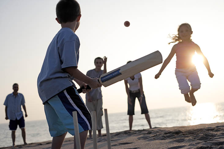 Strandcricket in Grossbritannien bei Sonnenuntergang, mit Kindern und Holzstümpfen im Sand.