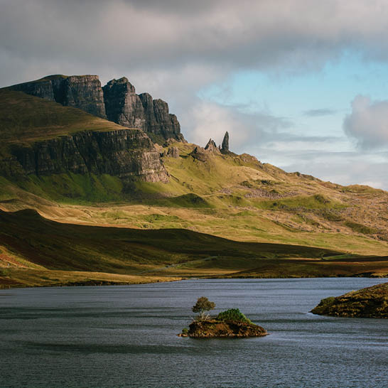 Landschaft auf der Isle of Skye mit See, kleiner Insel und markanten Felsformationen.