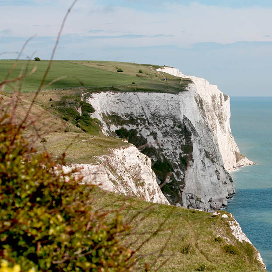 Weisse Kreideklippen von Dover über dem Meer mit grüner Graslandschaft.
