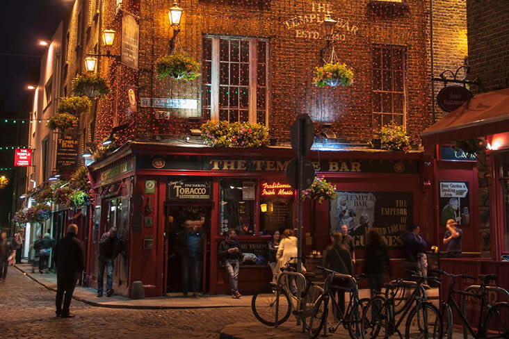 Temple Bar in Dublin bei Nacht mit roter Fassade, Lichterkette und lebhafter Strassenstimmung.