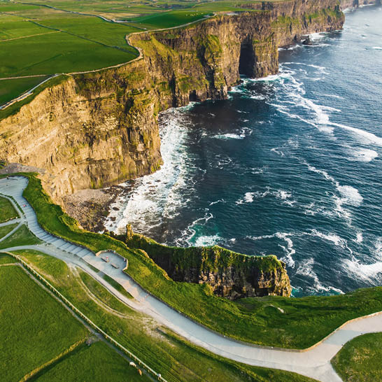 Steile Cliffs of Moher mit hohen Felsen, grünen Wiesen und kraftvollen Atlantikwellen.