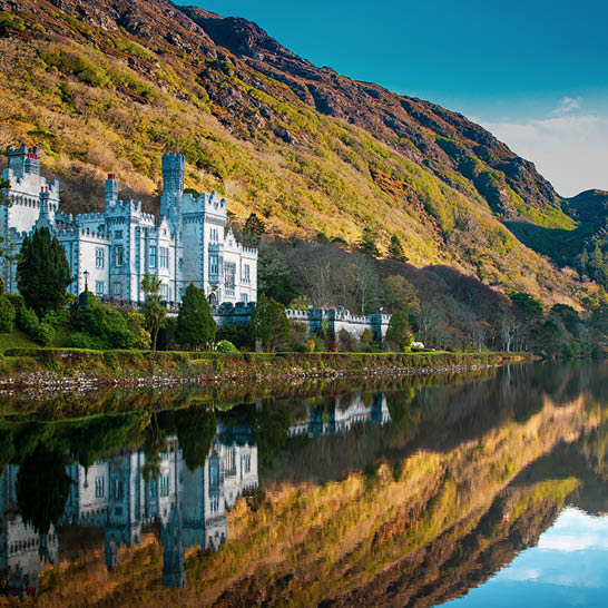 Kylemore Abbey vor bewaldeten Hügeln, spiegelnd im ruhigen See – ikonisches Irland‑Motiv.