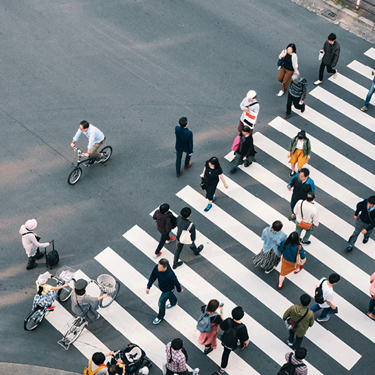 Un groupe de personnes traverse une rue animée au Japon, entouré de bâtiments et de panneaux publicitaires colorés.