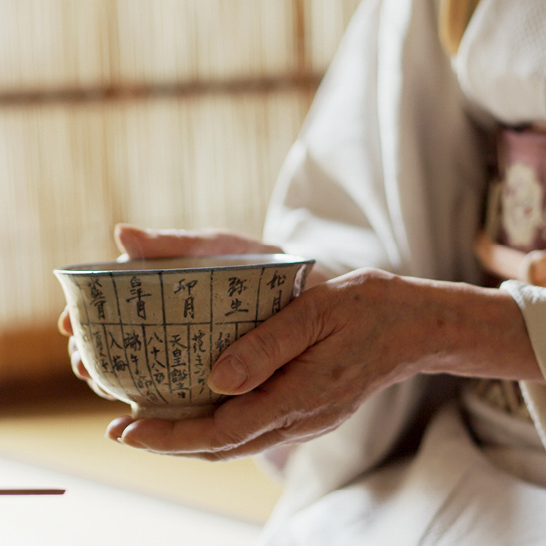 Une personne tenant un bol de thé japonais, avec une ambiance tranquille et traditionnelle en arrière-plan.
