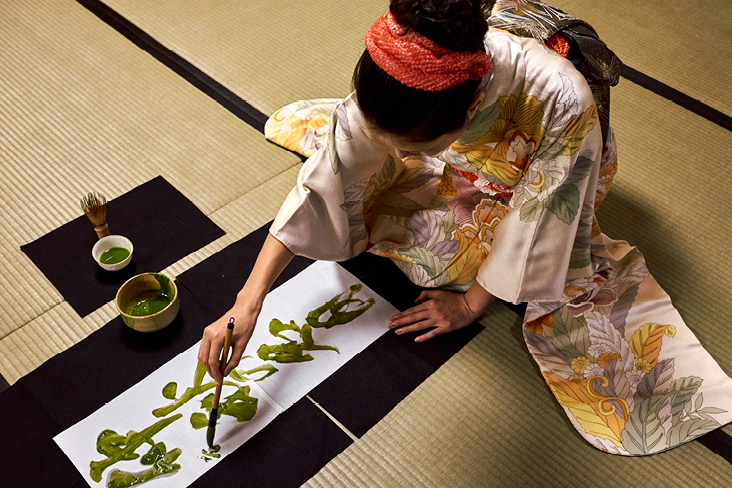 Une femme en kimono peint sur une feuille de papier, illustrant la culture japonaise avec élégance et créativité.