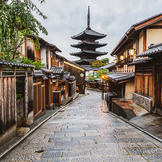 Une rue à Kyoto avec une pagode traditionnelle en arrière-plan, entourée de verdure et de bâtiments japonais.