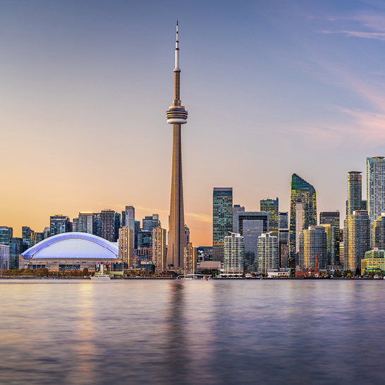 Skyline von Toronto mit dem CN Tower und dem Rogers Centre im warmen Abendlicht, gespiegelt im ruhigen Wasser des Lake Ontario.