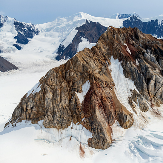 Massiver Berggipfel im Yukon National Park, umgeben von Schnee‑ und Eisfeldern in einer rauen, hochalpinen Landschaft.