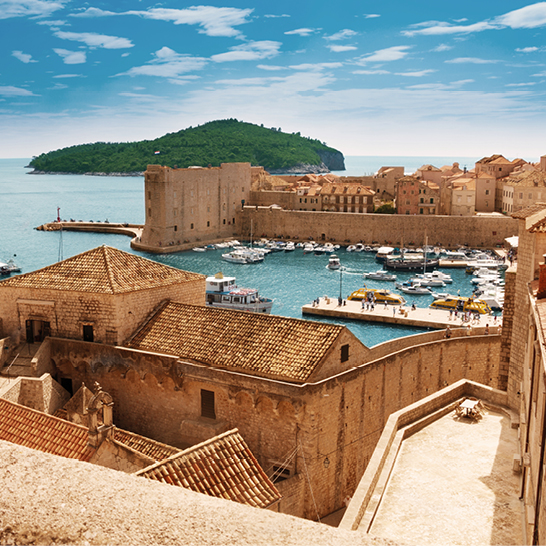 Historische Altstadt von Dubrovnik mit Stadtmauern aus Stein, terrakottafarbenen Dächern und Blick auf den Hafen.