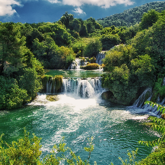 Mehrstufiger Wasserfall im Nationalpark Krka, umgeben von dichter Vegetation und türkisfarbenem Wasser.