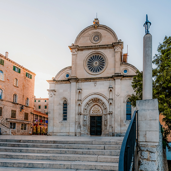 Fassade der Šibenik‑Kathedrale mit Rosettenfenster, steinernem Portal und umliegenden historischen Gebäuden.
