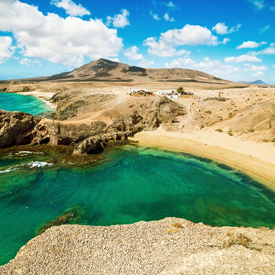 Une scène idyllique à Playa Papagayo, sur l'île de Lanzarote : la plage, une petite étendue d'eau et une montagne impressionnante au loin.