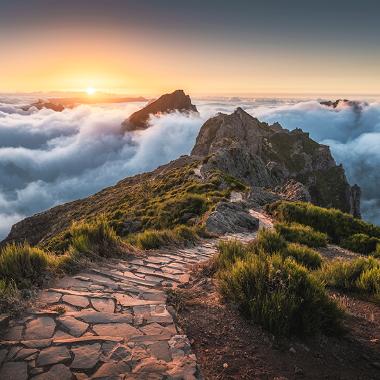 Un chemin de montagne s'élevant vers le sommet, avec des nuages en toile de fond.