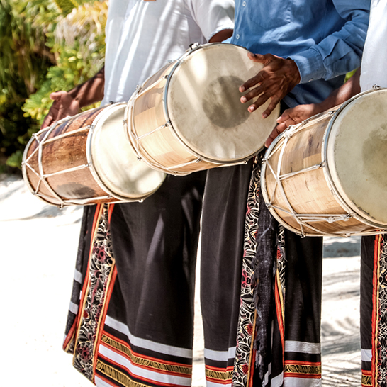 Am Strand spielt eine Gruppe von Männern rhythmisch auf ihren Trommeln und schafft eine lebhafte Atmosphäre.