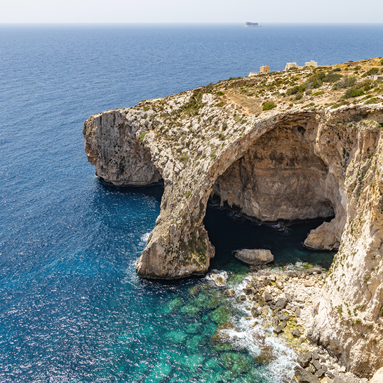 Kalksteinfelsen und natürlicher Bogen der Blue Grotto auf Malta, umgeben von türkisblauem Meer.